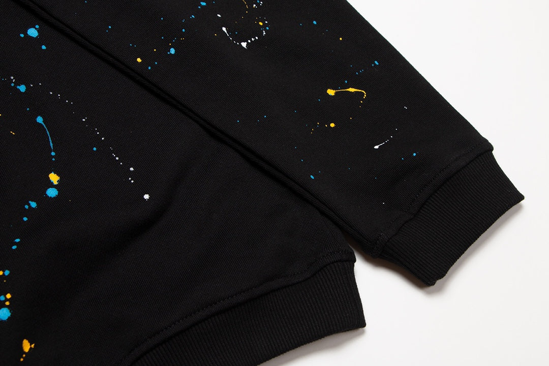 Sweat-shirt noir à motif de cœurs chromés, coulures de peinture et croix jaune.