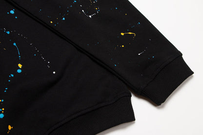 Sweat-shirt noir à motif de cœurs chromés, coulures de peinture et croix jaune.