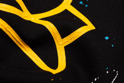 Sweat-shirt noir à motif de cœurs chromés, coulures de peinture et croix jaune.